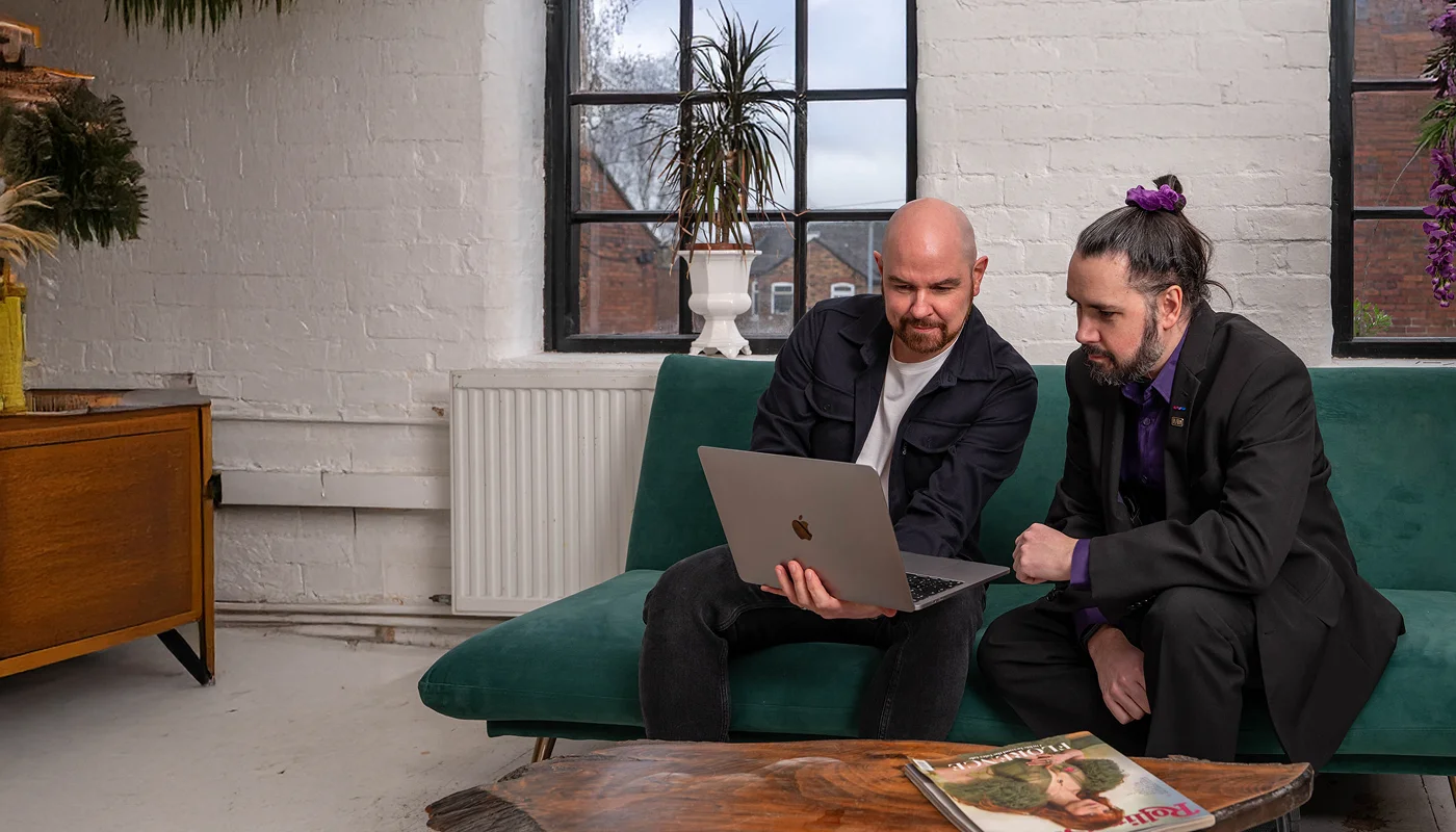 web developers sat on a casual sofa reviewing a website on a laptop