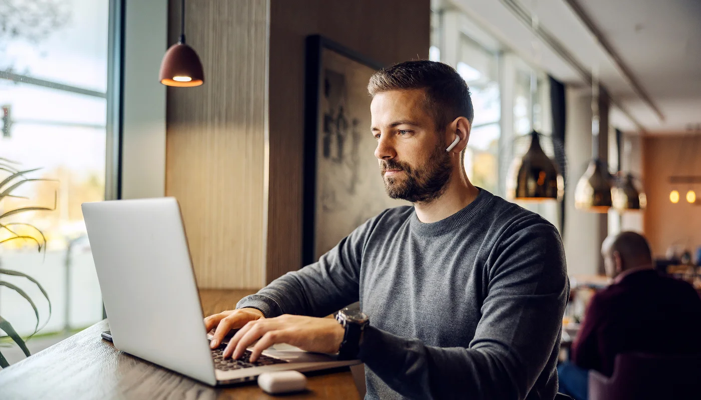 man in coffee shop using laptop to research a wordpress care plan