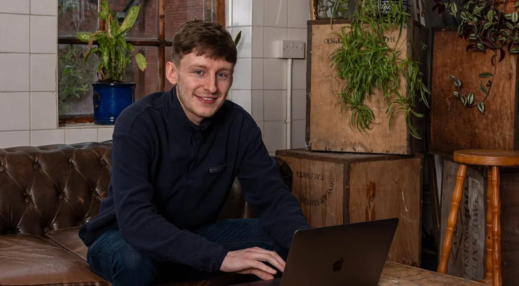 Yellow Circle developer smiling at camera with laptop on coffee table