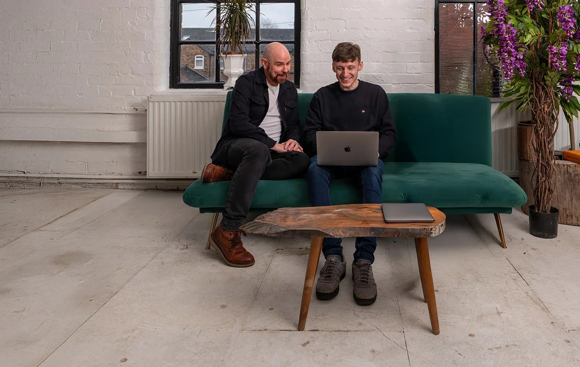 website maintenance team working on a laptop sat on a green sofa